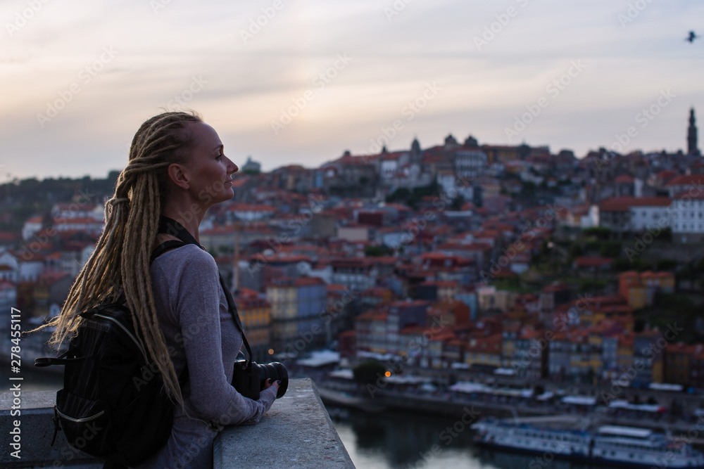 Young woman standing with camera in old town during dusk, Porto, Portugal. Tourism and travel.