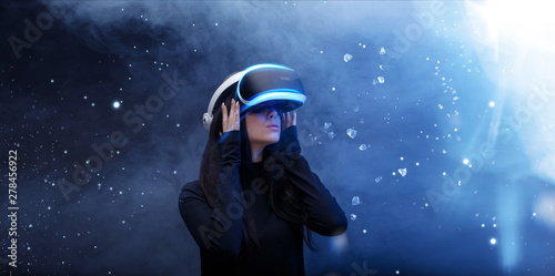 Beautiful woman over blue magic light background. Girl in glasses of virtual reality. Augmented reality, game, hobby, future technology concept. VR.