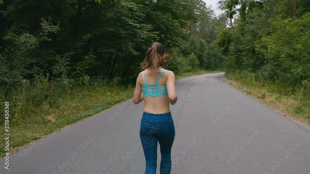 Runner woman running at road in forest in slowmotion. outdoors fitness. Shot with steadicam. Morning running concept. Runner woman running at road in forest in slowmotion. outdoors fitness. Shot with steadicam. Morning running concept.
