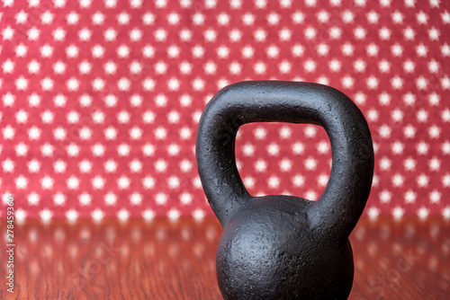 Fototapeta Naklejka Na Ścianę i Meble -  Rustic black kettlebell on a wood floor against a patterned backdrop of red and white