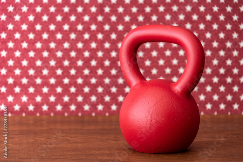 Fototapeta Naklejka Na Ścianę i Meble -  Large red kettlebell on a wood floor against a patterned backdrop of red and white