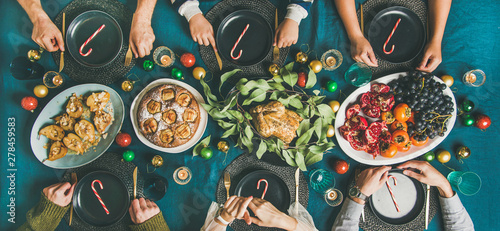 Company of friends gathering for Christmas or New Year party dinner at festive table. Flat-lay of people sitting with plates and ready to start celebrating holiday together, top view, wide composition