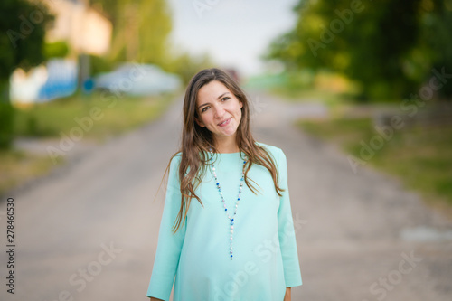 Pregnant girl in a turquoise dress. Pregnant woman in day dress strolling in the park. The girl smiles. comfortable clothes for pregnant women.