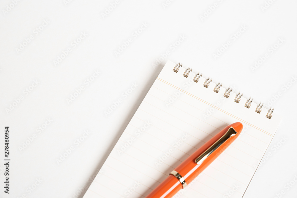 A shiny orange fountain pen together with a spiral-bound notebook. A shiny orange fountain pen together with a spiral-bound notebook.