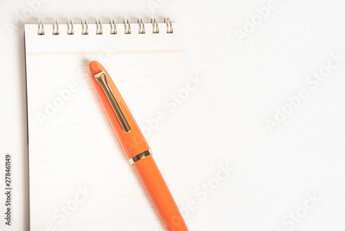 A shiny orange fountain pen together with a spiral-bound notebook. photo