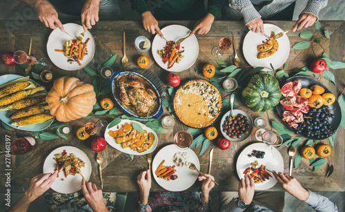 Thanksgiving, Friendsgiving holiday celebration. Flat-lay of friends eating meals at Thanksgiving Day table with turkey, pumpkin pie, roasted vegetables, fruit, rose wine, top view