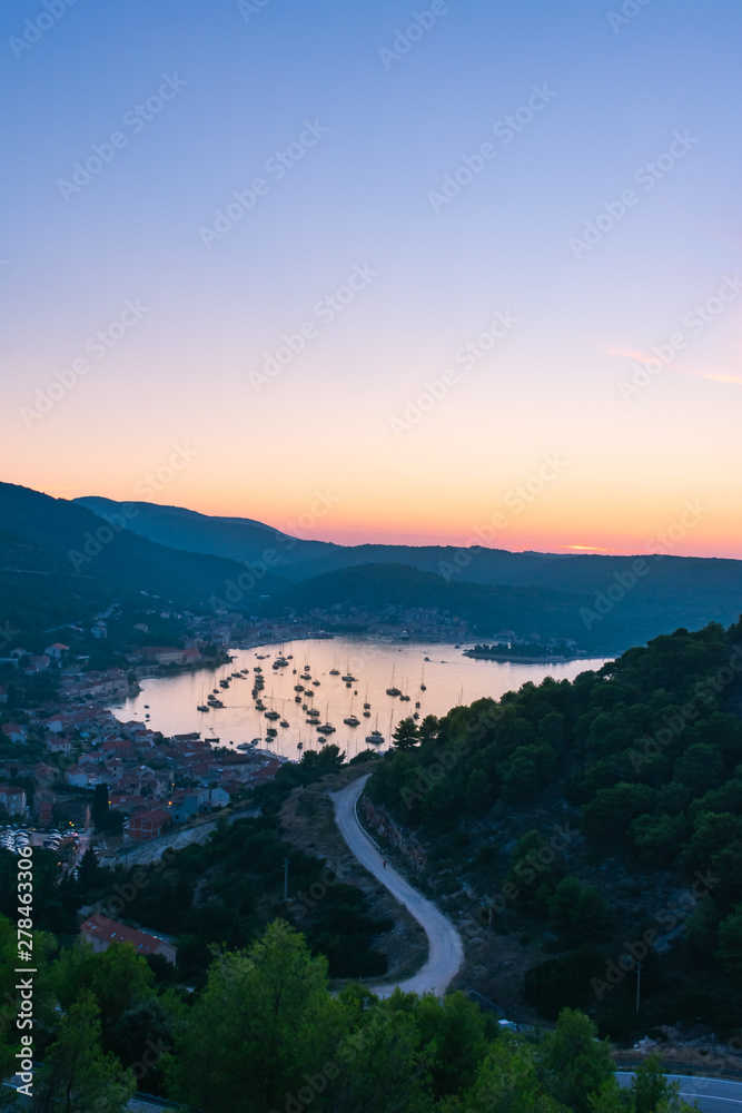 Landscape and top view of the old historic city of Vis and the harbor with moored sailing boats and yachts during a beautiful sunset in summer, Vis island, Croatia, Europe