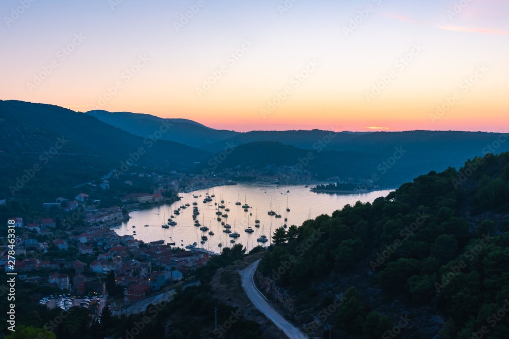 Obraz premium Landscape and top view of the old historic city of Vis and the harbor with moored sailing boats and yachts during a beautiful sunset in summer, Vis island, Croatia, Europe