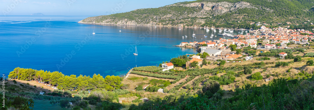 Panoramic view of a blue bay with the picturesque town of Komiza with red rooftops, white sailing boats on a summer morning viewed from above, Adriatic sea, mediterranean, Vis island, Croatia, Europe