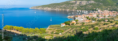 Panoramic view of a blue bay with the picturesque town of Komiza with red rooftops, white sailing boats on a summer morning viewed from above, Adriatic sea, mediterranean, Vis island, Croatia, Europe © IKA