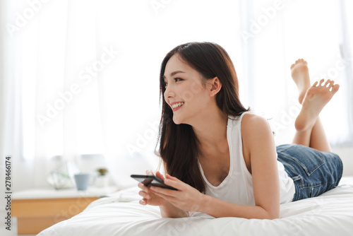 Happy woman relaxing using and talking by smartphone on the bed at home.technology and communication concept