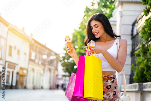 Gorgeous girl with shopping bags and ice cream enjoying shopping in the city 
