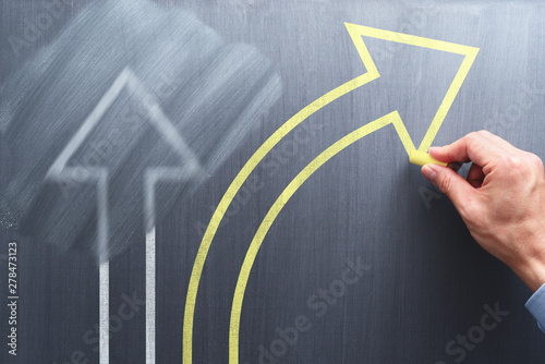 Changing business management concept. Businessman erasing white arrow and drawing yellow arrow on chalkboard.
