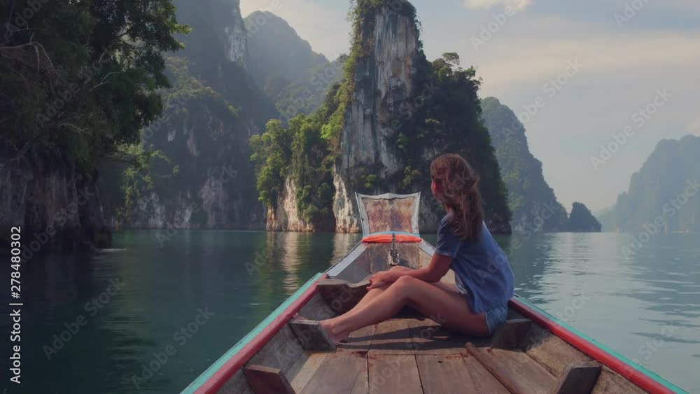 Lifestyle video of pretty travel woman sitting in wood long tail boat on tropical limestone cliffs . Explore and vacation concept. Khao Sok lake, Thailand.
