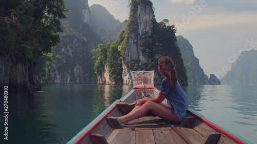 Lifestyle video of pretty travel woman sitting in wood long tail boat on tropical limestone cliffs . Explore and vacation concept. Khao Sok lake, Thailand. photo