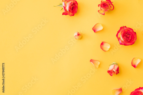 Floral greeting card. Flat lay of red rose buds, petals scattered over orange background. Copy space.