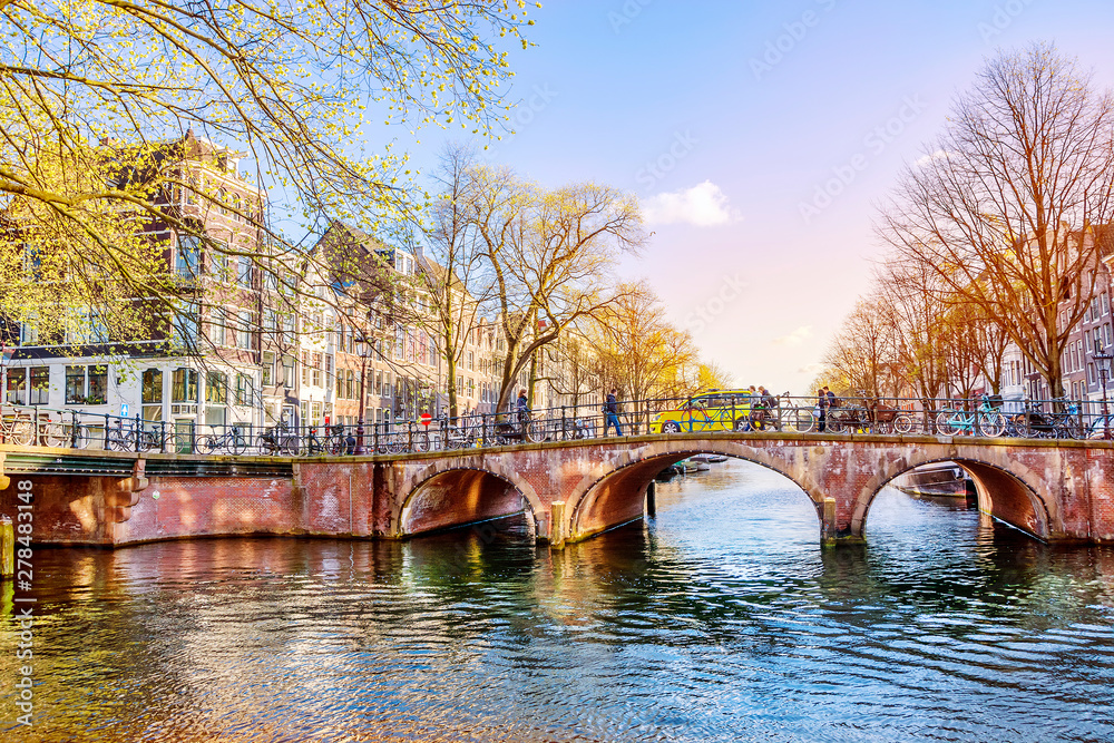 Stone arched bridge over Amsterdam canal in spring sunny evening, Netherlands