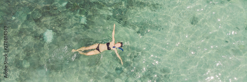 Aerial top view of woman snorkeling from above, girl snorkeler swimming in a clear tropical sea water with corals during summer vacation BANNER, LONG FORMAT