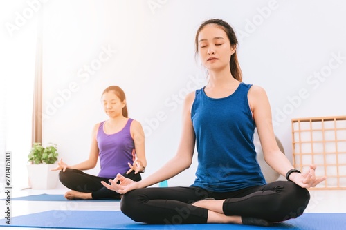 Asian beautiful woman group meditation and sitting in yoga lotus position in yoga classroom background.Concept of exercise for good health lifestyle.