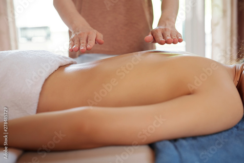 Close-up image of professional reiki healer treating back of female patient in health spa center