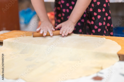 Hands working with bread dough recipe preparation. Female hands making dough. Women's hands roll out the dough. Mom rolls dough on a kitchen board with a rolling pin © donikz