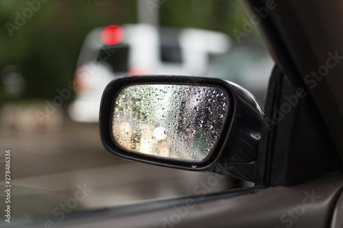 Car side mirror glass with water droplets from rain - driver's side rear view on rainy day