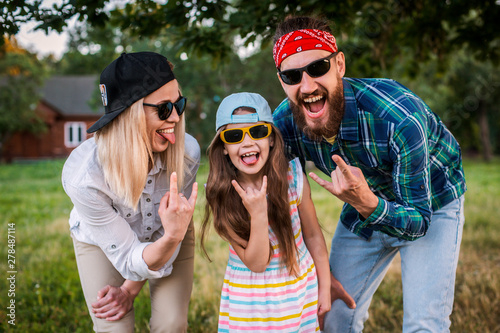 Funny man, woman and child with protruding tongues in rocker style scream.