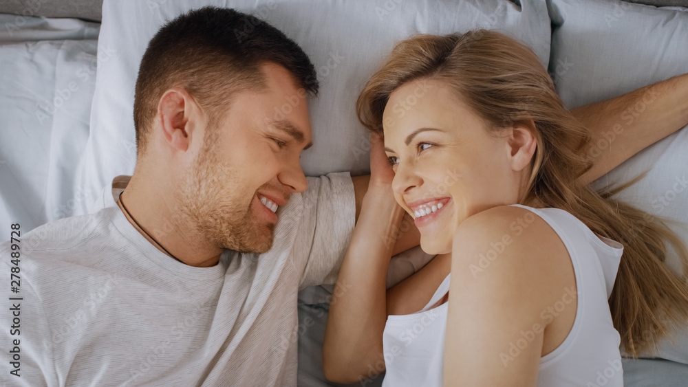 Happy Young Couple Cuddling Together in the Bed, Young Woman is Pregnant and Loving Partner Touches and Caresses Her Tenderly. Top View Shot. Happy Young Couple Cuddling Together in the Bed, Young Woman is Pregnant and Loving Partner Touches and Caresses Her Tenderly. Top View Shot.