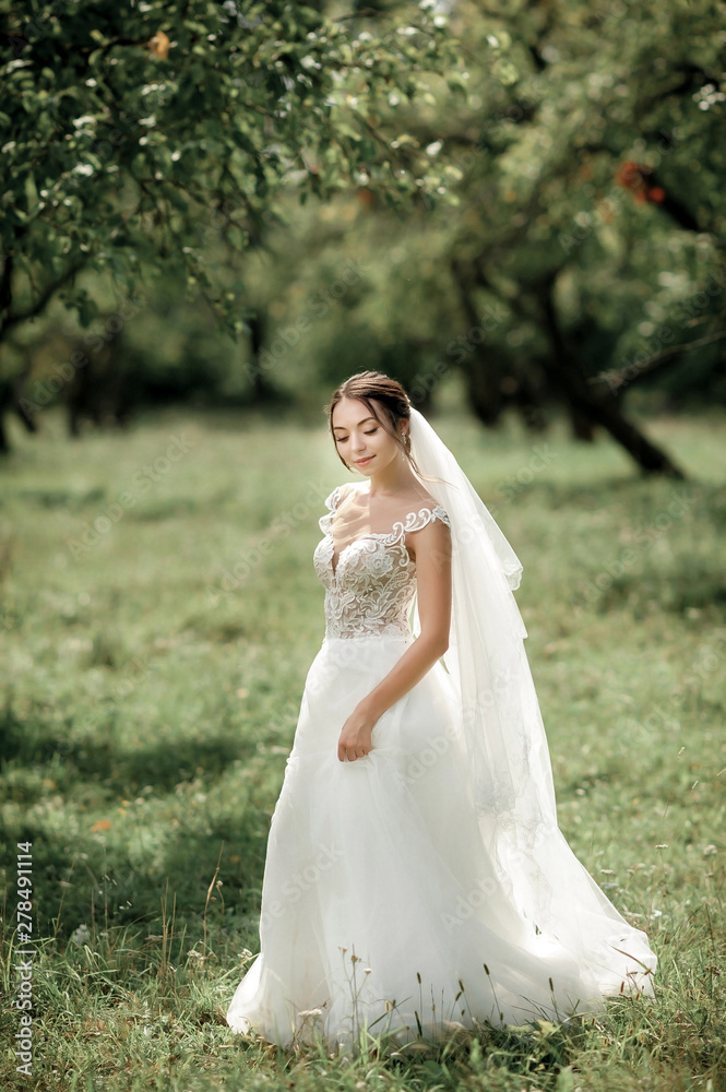 bride posing in a green park; girl in a white dress on a background of green