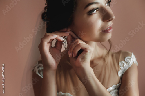 girl in a wedding dress at home; preparing the bride for the holiday; bride in a wedding dress against a dark wall