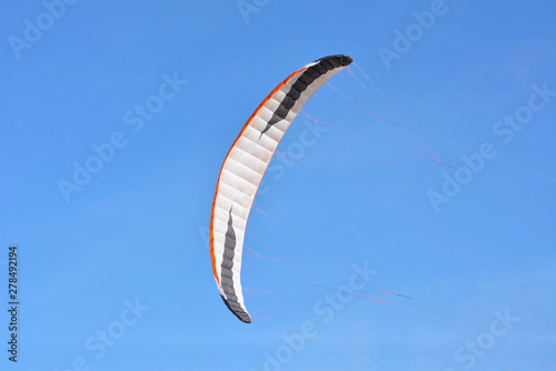 Big white, black and orange bow kite flying in front of clear blue sky