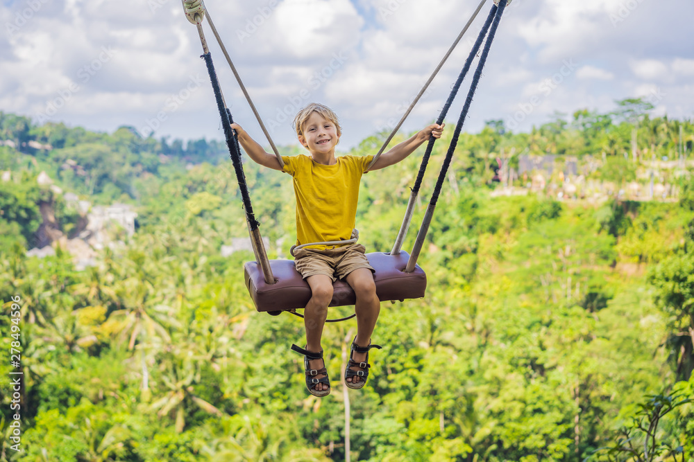 Young boy swinging in the jungle rainforest of Bali island, Indonesia. Swing in the tropics. Swings - trend of Bali. Traveling with kids concept. What to do with children. Child friendly place