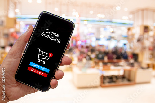 Person using smartphone buying and making a payment digitally via application on blur shopping mall background - internet online home shopping concept