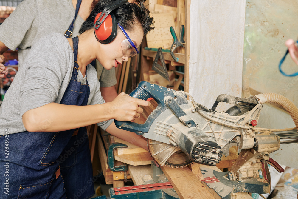 Professional young Asian female carpenter in ear muffs using circular saw  when cutting pine wooden planks Stock Photo | Adobe Stock