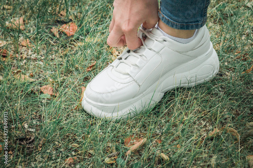 Close up legs of woman dressed in jeans and sneakers step on the grass.