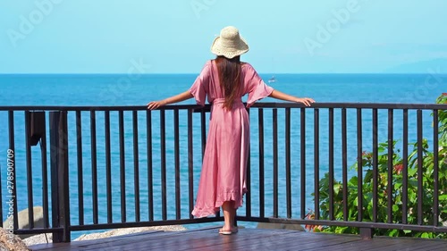 Gorgeous Styllish Female in Summer Dress and Hat Standing By Fence and Enjoying View of Tropical Paradise photo