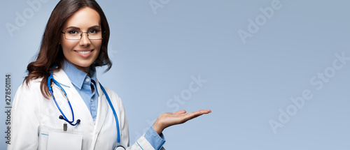Female doctor showing something or blank copy space for slogan or sign text, isolated against grey background
