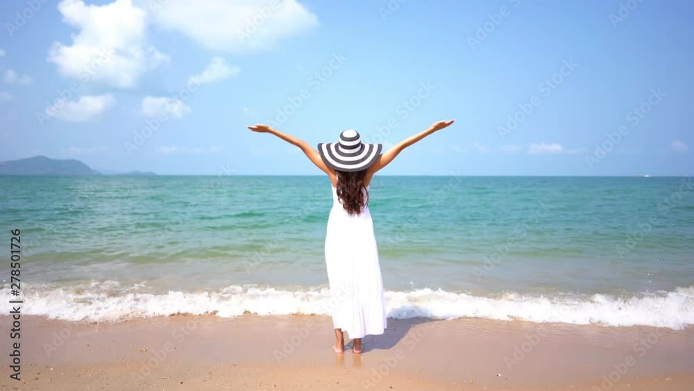 A young woman dressed in white stands on a beach, arms raised in joy. A young woman dressed in white stands on a beach, arms raised in joy.