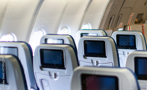 Modern aircraft interior with seats and blank touch entertainment screens displays. Concept of fast and comfort travel and new technologies.