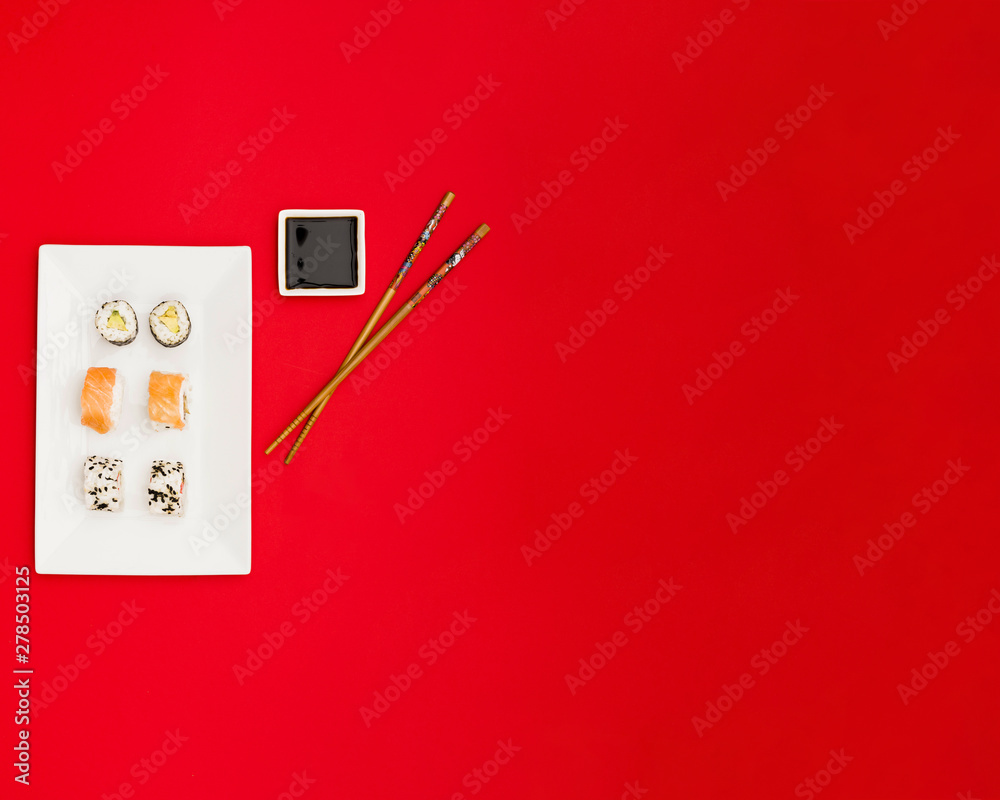 Top view of delicious rolls with soya sauce and chopsticks over bright red background Top view of delicious rolls with soya sauce and chopsticks over bright red background
