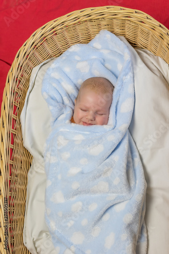 Top view of beautiful newborn boy sleeping in knit basket. The child smiles in his sleep. Vertically. 