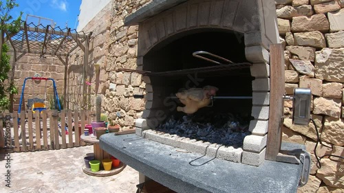 Rotisserie Chicken rotating in a wood and charcoal fire brick bbq grilling in fast forward photo