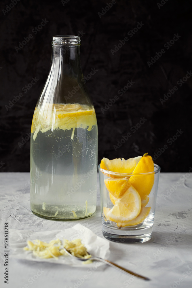 Fototapeta premium Homemade refreshing infused detox water or lemonade in glass bottles with grated ginger and lemon on dark background close-up with copy space for text.Healthy vegan drink concept.Selective focus