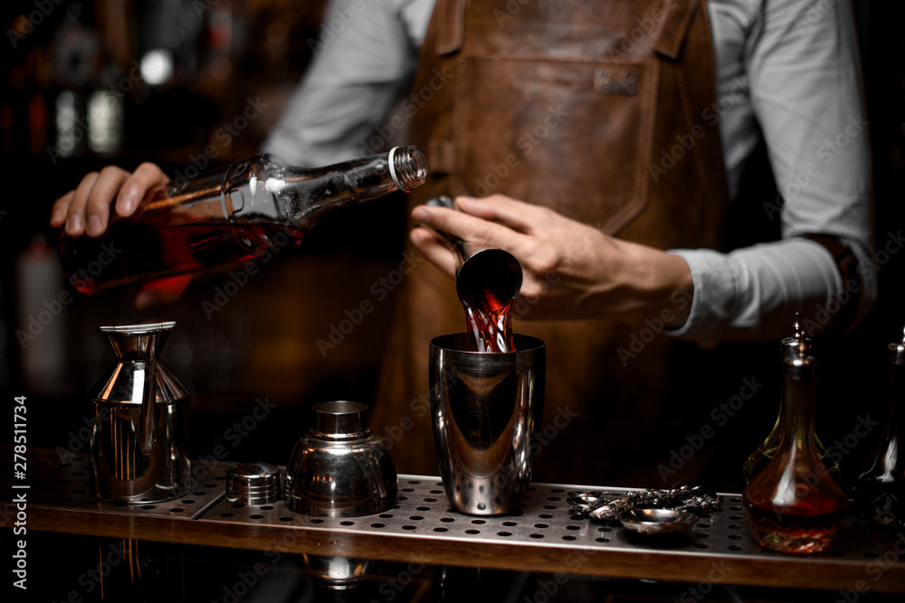Male bartender pouring an alcoholic drink from the steel jigger to the cocktail shaker