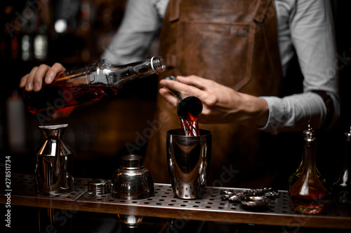 Male bartender pouring an alcoholic drink from the steel jigger to the cocktail shaker