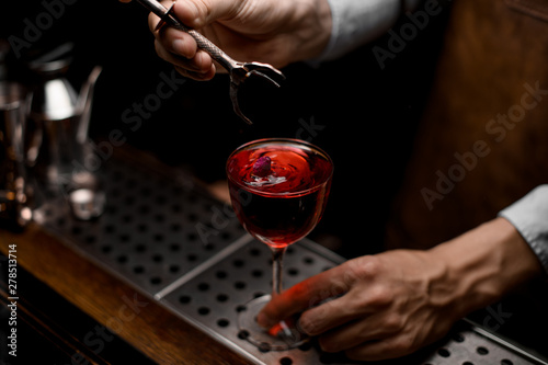 Male bartender putting a little rose bud to the red cocktail in the glass