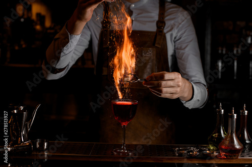 Bartender fire a decor for a delicious red cocktail in the glass