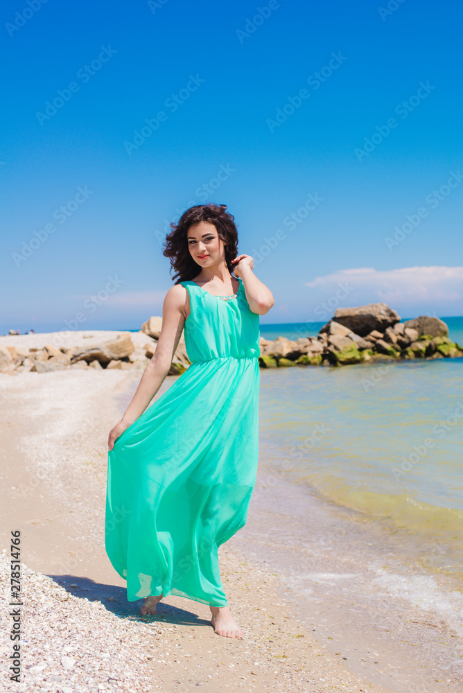 Young beautiful girl in dress on the beach in summer. The girl in the blue sea on the sand Young beautiful girl in dress on the beach in summer. The girl in the blue sea on the sand