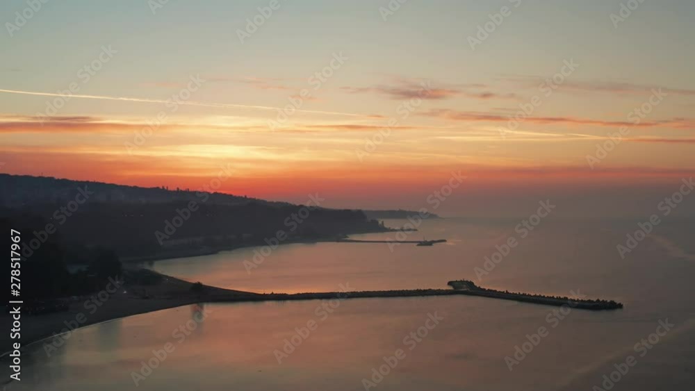 Bright sunrise of the sun over the sea and the beautiful coast of the sea town scenic aerial view from drone slide up. Pink-orange dawn of the sun in the summer early morning in the sky. Relax Bright sunrise of the sun over the sea and the beautiful coast of the sea town scenic aerial view from drone slide up. Pink-orange dawn of the sun in the summer early morning in the sky. Relax