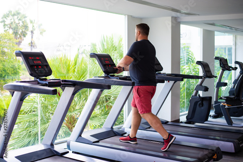 full male runs on a treadmill in a gym. concept of weight loss and sport. back view.